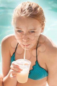 Little blond girl drinks cocktail in swimming pool, vintage toned vertical photo filter effect