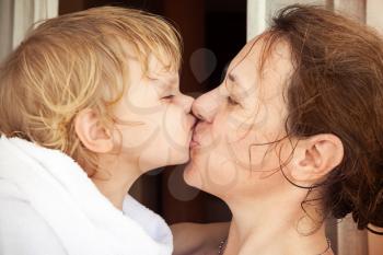 Young happy mother kisses her cute baby girl in white towel after taking a bath