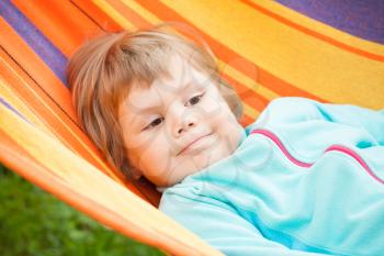 Cute blond baby girl lying in striped hammock, outdoor closeup portrait