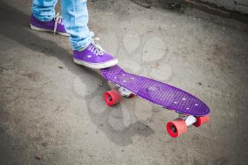 Young skateboarder feet in gumshoes and jeans standing on his skate. Closeup fragment of skateboard and feet, photo with retro tonal correction filter