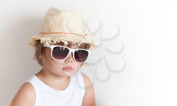 Cute Caucasian little girl in straw hat and sunglasses over white wall background
