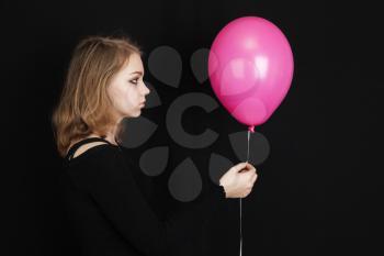 Studio profile portrait of teenage Caucasian blond girl with pink balloon over black background