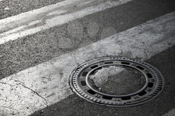 Sewer manhole cover on dark asphalt road with pedestrian crossing marking