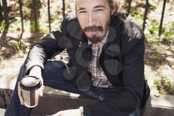 Bearded Asian man with coffee in paper cup, outdoor portrait with selective focus and tonal correction photo filter effect