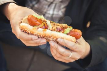 Man holds fresh hot dog in hands, closeup photo with selective focus