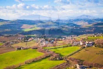 Rural panorama of Italian countryside. Province of Fermo, Italy. Villages and fields on hills under blue cloudy sky