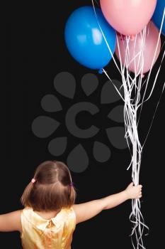 Caucasian blond little girl with colorful balloons, rear view over black background