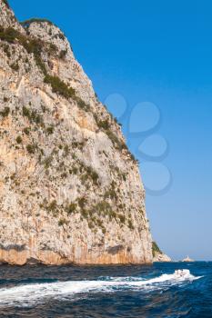 Small pleasure motorboat with ordinary tourists go near coastal rocks of Capri island, Italy