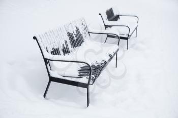 Two outdoor metal benches covered with snow in winter park. Turku, Finland