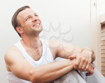 Portrait of Young smiling Caucasian man in white shirt sitting on balcony and looking up