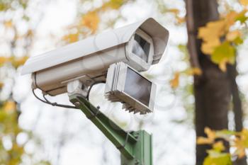 Close-up photo of an outdoor surveillance camera with motion detector in autumnal park