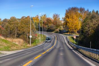 Car goes down the turning rural highway in autumn season, Norwegian countryside