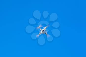 White quadcopter in blue sky, compact drone controlled by wireless remote, bottom view