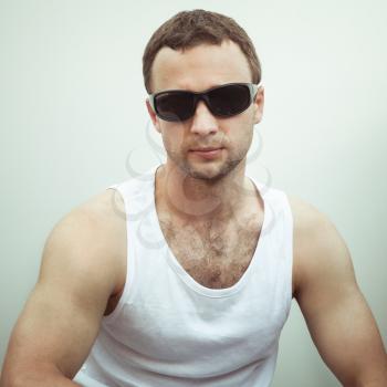 Portrait of Young sporty serious European man in white shirt and black sunglasses, vintage toned square photo