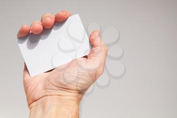 Male hand holds white empty card over gray wall background, close up photo, selective focus
