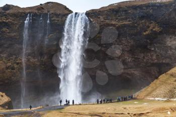 Tourists walk near Seljalandfoss waterfall, natural landmark of Iceland