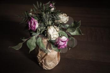 Bouquet of dried red and white roses stands on wooden table, closeup low key photo with soft selective focus and tonal correction filter