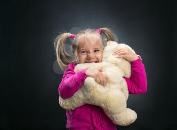 Little cute girl holds toy bear on grey