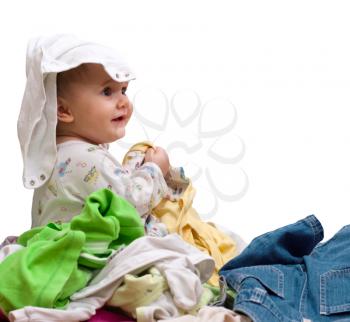 Happy baby girl playing in heap of baby's wear. Isolated