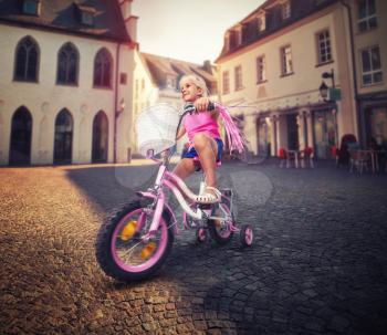 Cute little girl cycling on pink bike on the street