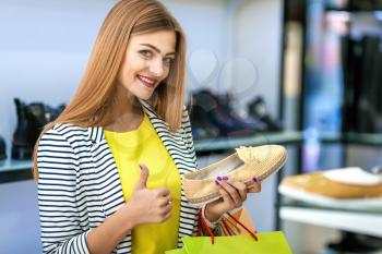 Happy woman holds one flat shoe and shows thumb up while shopping