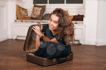Young woman trying to climb into a suitcase. Vintage travel concept.