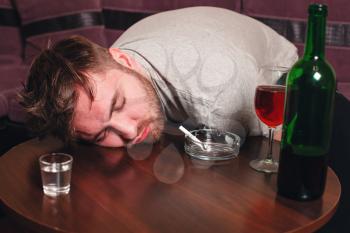 Drunk man sleep on wooden table. Alcohol and ashtray with cigarette  on table.