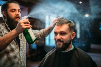Hairdresser water with spray hair of the client man in black salon cape. Male person visit barbershop