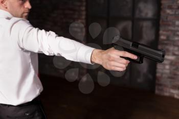 Serious hired murderer in red tie aims a gun. Professional secret agent concept. Assassin with guns, wallpaper, background or poster. Contract killer with weapon