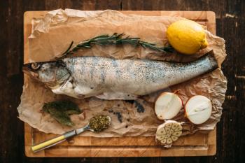 Fresh fish preparation ingredients, herbs, spices, onion and garlic, lemon on cutting board covered with parchment paper, top view