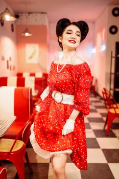 Pinup woman in red dress with white polka dots, vintage style. Retro cafe interior with checkerboard  floor