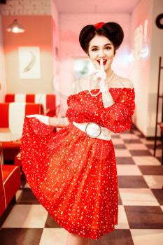 Pretty pin-up woman with make-up, red dress with white polka dots, vintage style. Retro cafe interior with checkerboard  floor