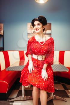 Glamour pinup girl with makeup, retro cafe interior, 50 american fashion. Red dress with polka dots, vintage style