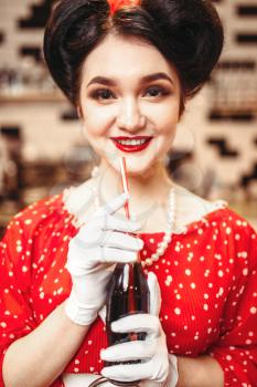 Pin up girl with make-up drinking popular carbonated drink, 50 american fashion. Red dress with polka dots, vintage style