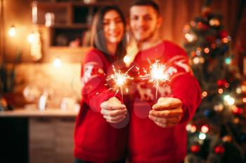 Love couple holds sparklers in hands, christmas romantic celebration. Man and woman celebrate xmas together