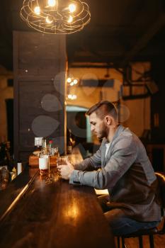 Man with bottle of alcohol beverage drinks at wooden bar counter. Customer leisures in pub, male person relax in a bar