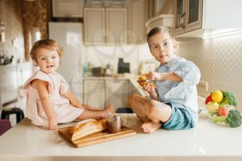 Two kids smears melted chocolate on bread, tasty sandwiches. Cute boy and girl cooking on the kitchen. Happy children prepares and tastes sweet dessert at the counter