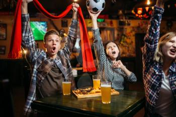 Football fans with scarf and ball in hands watching match and drinks beer in sports bar. Tv broadcasting, young friends leisures in pub, favorite team wins