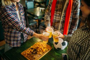 Football fans clink glasses with light beer in sports bar. Tv broadcasting, young friends celebrates win of the favorite team, success game celebration in pub