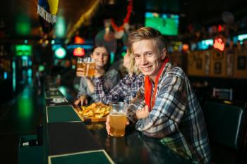 Football fans with glasses of beer at the counter in sports bar. Tv broadcasting, young friends celebrates win of the favorite team, success game celebration in pub