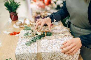 Female person ties a gold bow on gift box, handmade wrapping and decoration process. Woman wraps present on the table, decor procedure