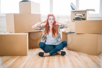 Tired woman sitting in yoga pose among cardboard boxes, housewarming. Relocation to new home