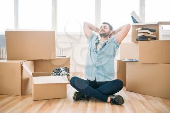 Thoughtful man sitting in yoga pose among cardboard boxes, housewarming. Relocation to new home