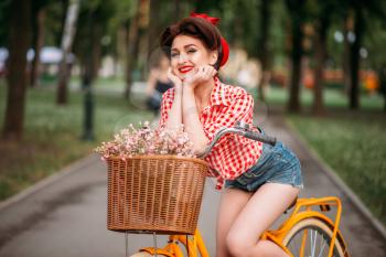 Pinup woman on bicycle with backet of flowers, vintage fashion. Pin-up style attractive girl
