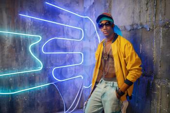 Black rapper in underpass neon light on background. Rap performer in club with grunge walls, underground music