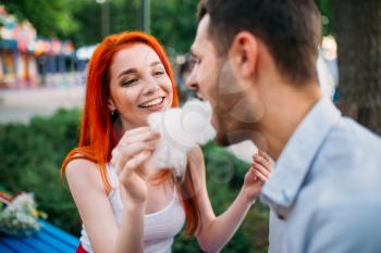 Smiling woman feeding man cotton candy. Romantic date of beautiful love couple in summer park, meeting outdoors
