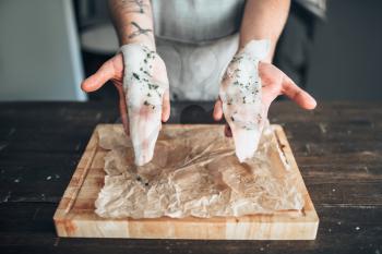 Male chef hands holds raw fish slices with spices over wooden cutting board closeup view. Seafood cooking. Fresh sea food preparation