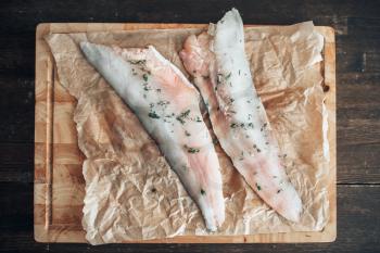 Raw fish slices with spices on cutting board covered with parchment paper, top view