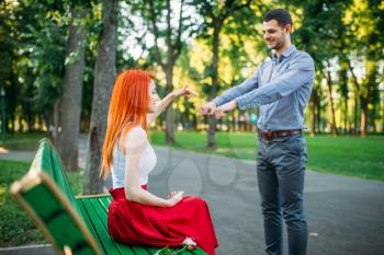 Romantic date of couple on a bench in summer park. Girl chooses in which hand surprise