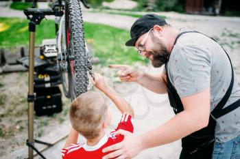 Bicycle mechanic show bike on stand to young boy. Cycle workshop outdoor. Bicycling and kids